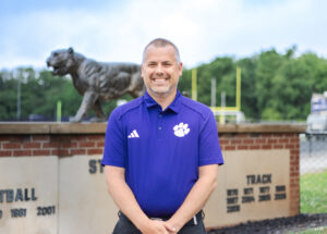 Man in purple shirt with white paw stands in front of the tiger stadium at Tiger Stadium