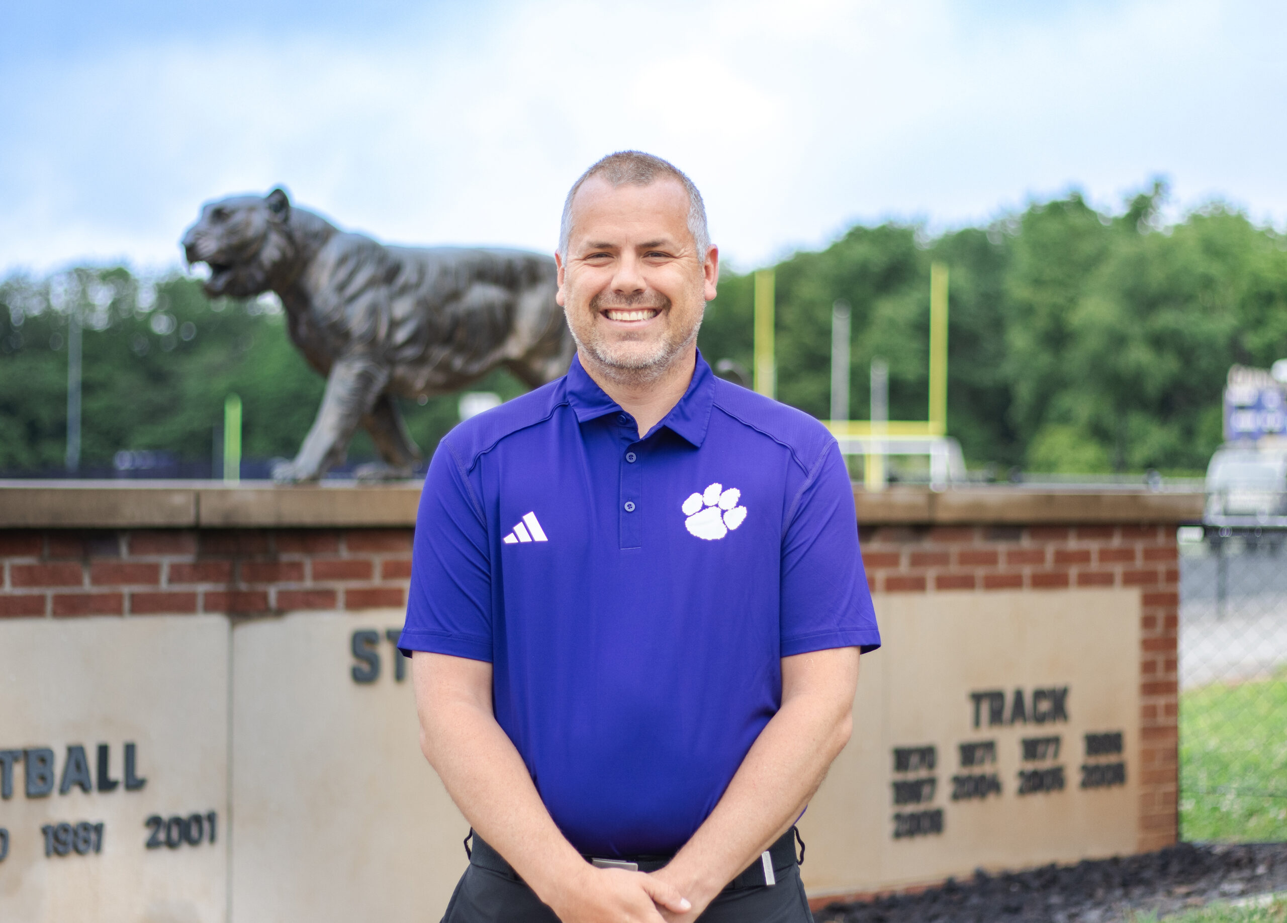 Man in purple shirt with white paw stands in front of the tiger stadium at Tiger Stadium