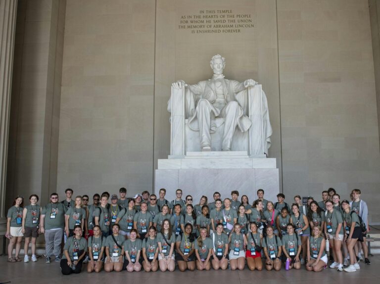 Students in green shirts stand in front of the Abraham Lincoln monument