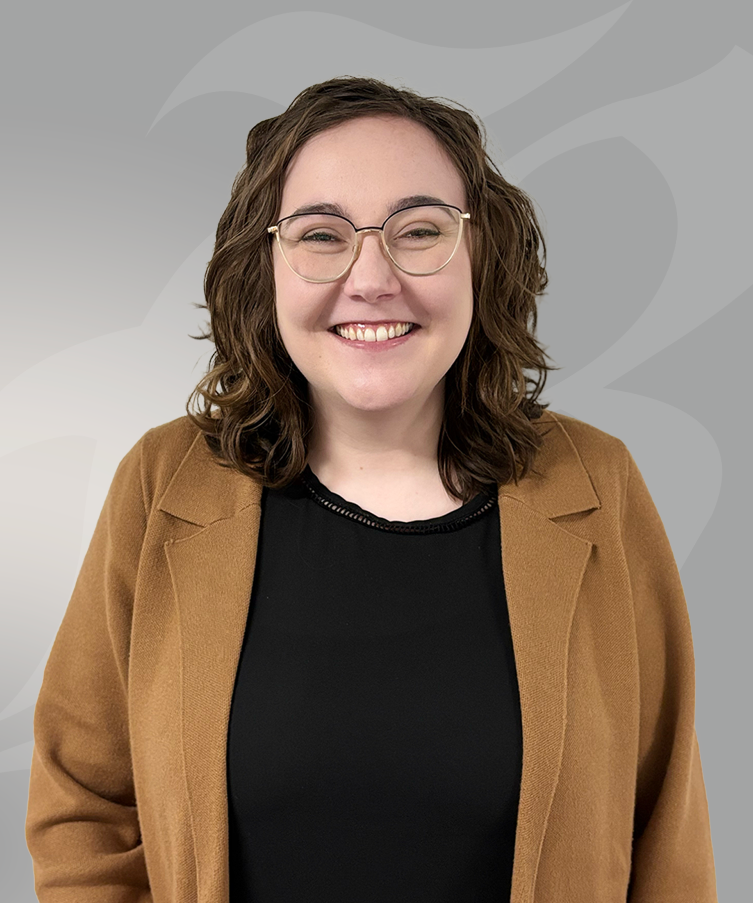 women standing in front of gray wall with black shirt and brown jacket on.