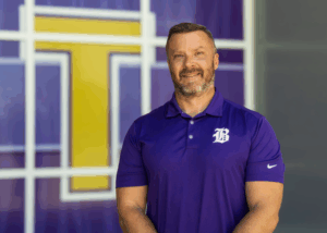 man in purple polo stands in front of the cafeteria windows